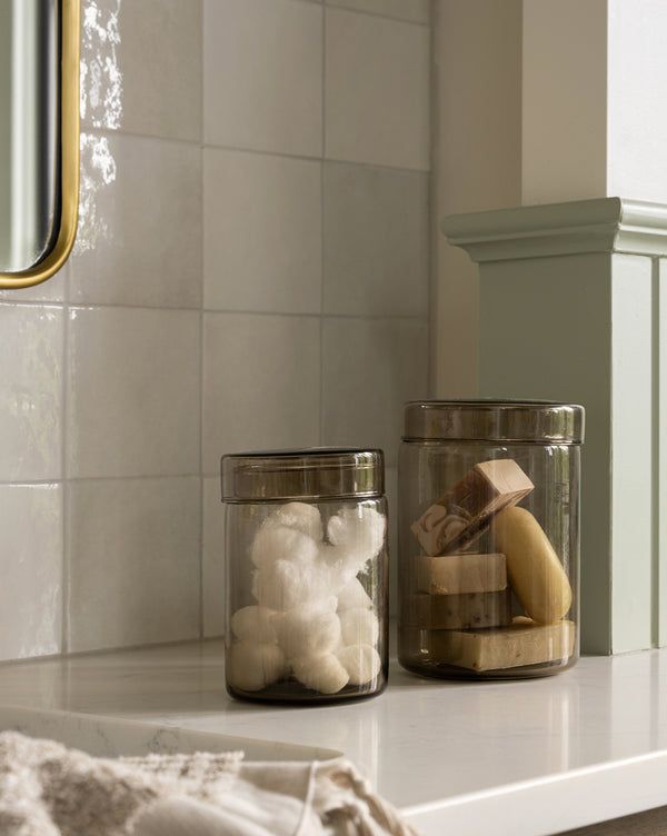 two jars filled with different types of items on top of a white counter next to a mirror