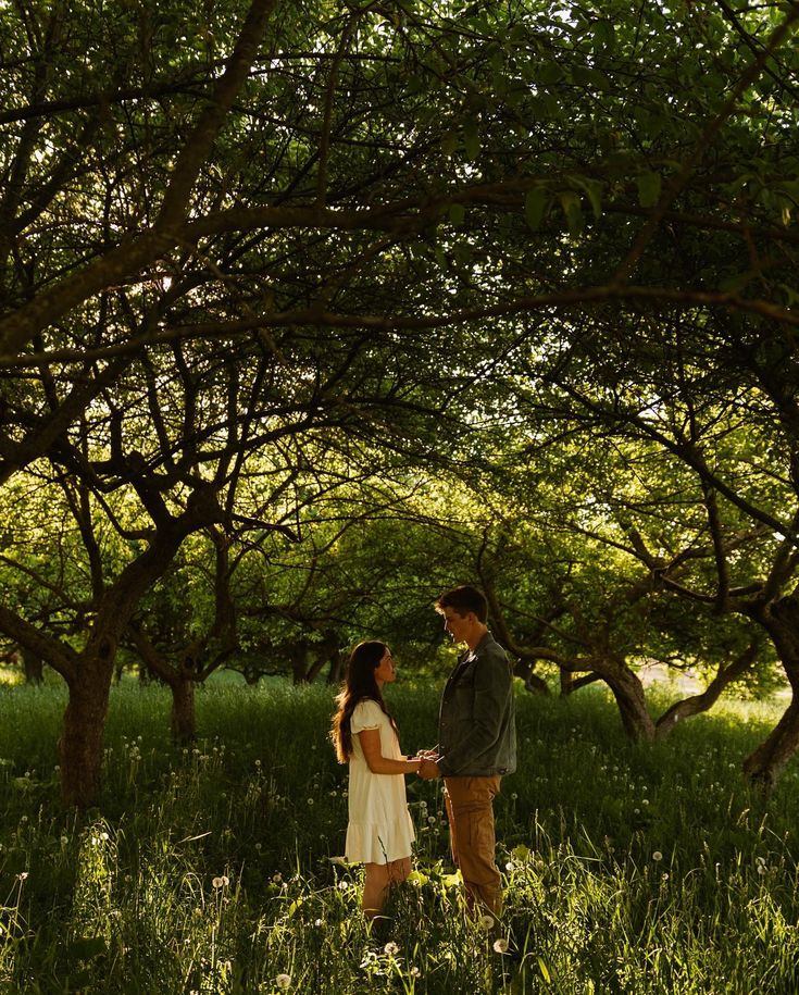 a man and woman standing in tall grass under trees