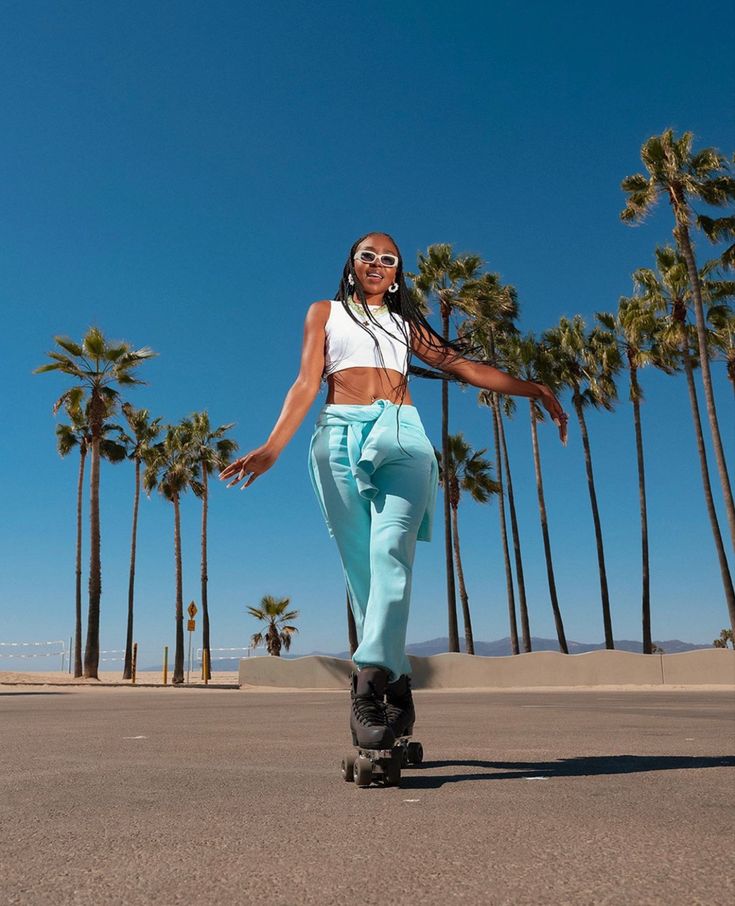 a woman riding a skateboard down the middle of a street next to palm trees