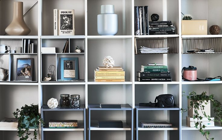 a book shelf with many books on top of it and plants in the bottom right corner