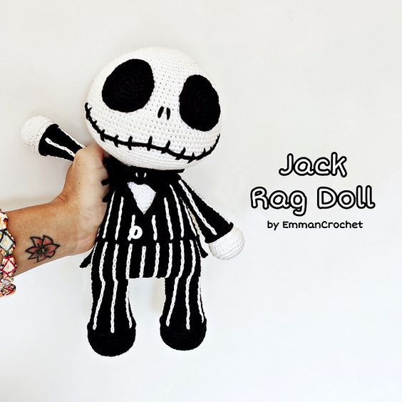 a hand holding a crocheted jack skellingy doll in front of a white background