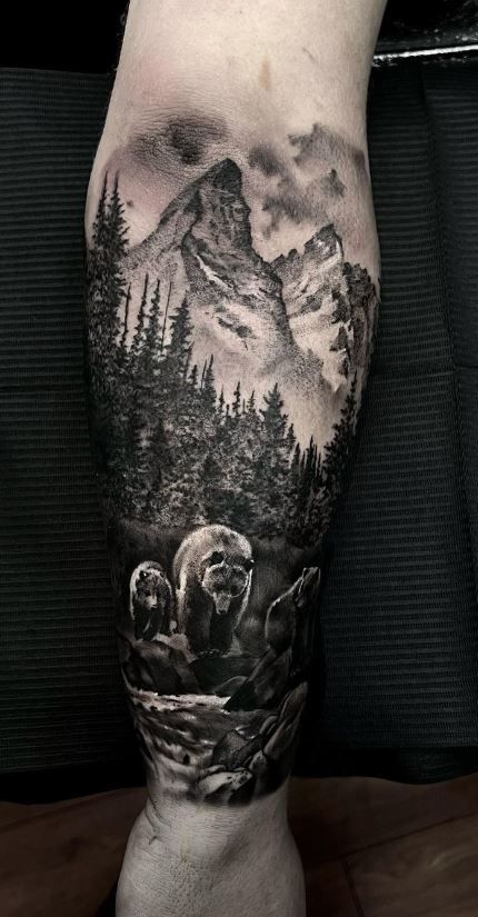 a man's leg with a bear and mountain scene on it, done by tattoo artist