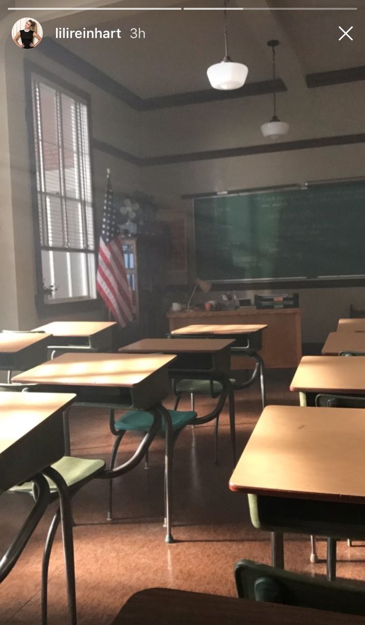 an empty classroom with desks and american flag on the chalkboard in the back