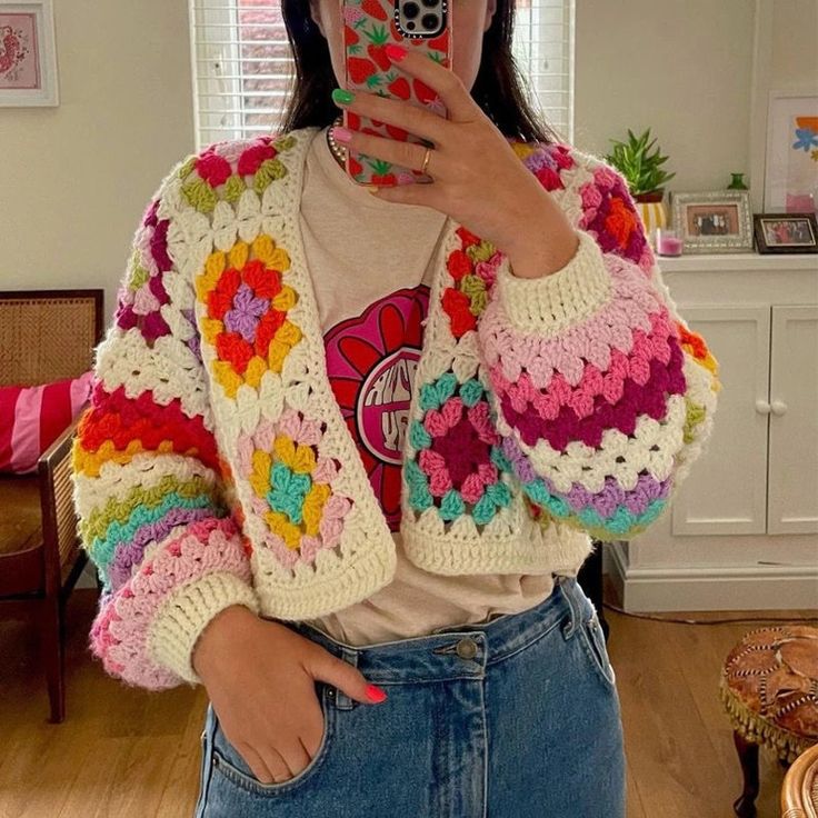 a woman taking a selfie with her cell phone in front of the camera and crocheted jacket on