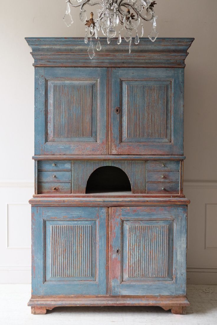 an old blue cabinet with a chandelier above it