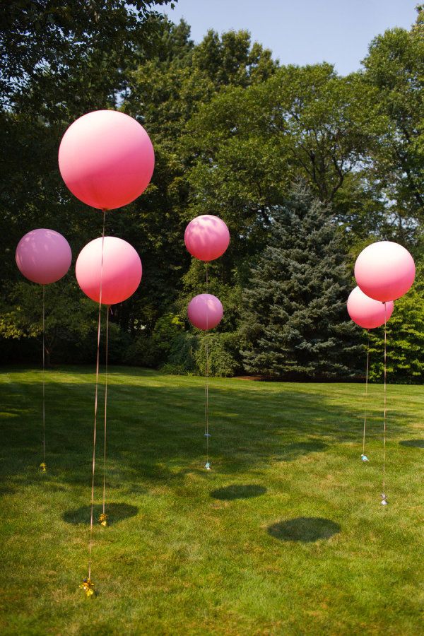 several pink balloons are floating in the air on green grass with trees in the background