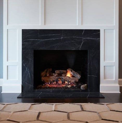 a fire place in a room with white walls and black marble surround it is lit