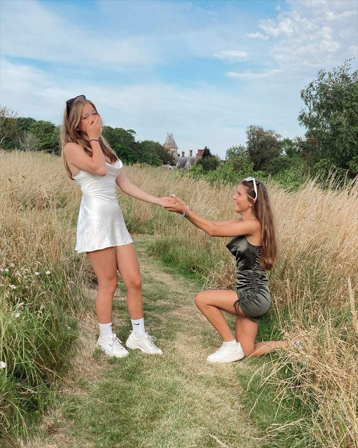 two young women in short dresses are touching hands with each other on the grass field