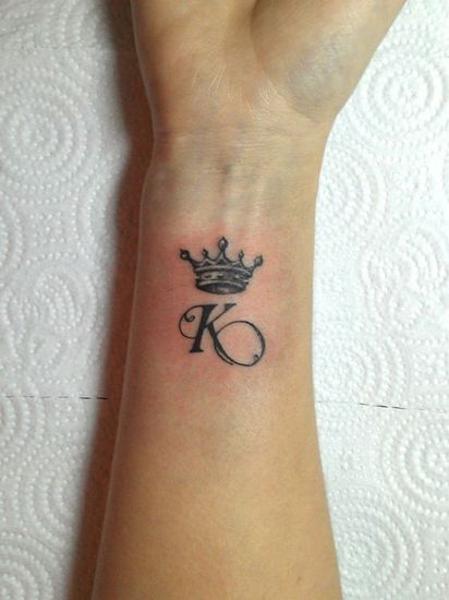 a small tattoo on the wrist of a woman with a crown and initial letter k