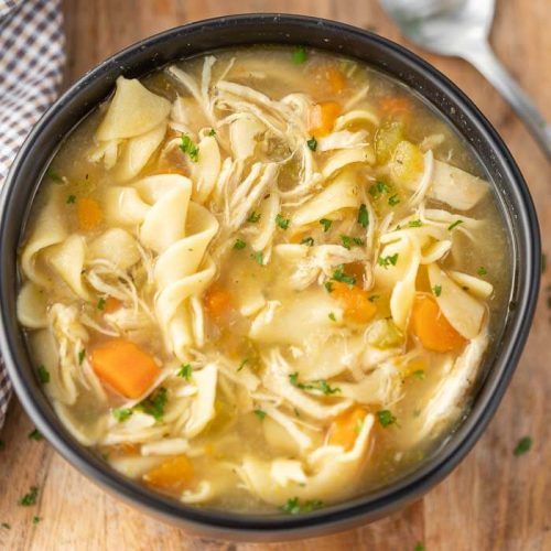 a bowl filled with chicken noodle soup on top of a wooden table