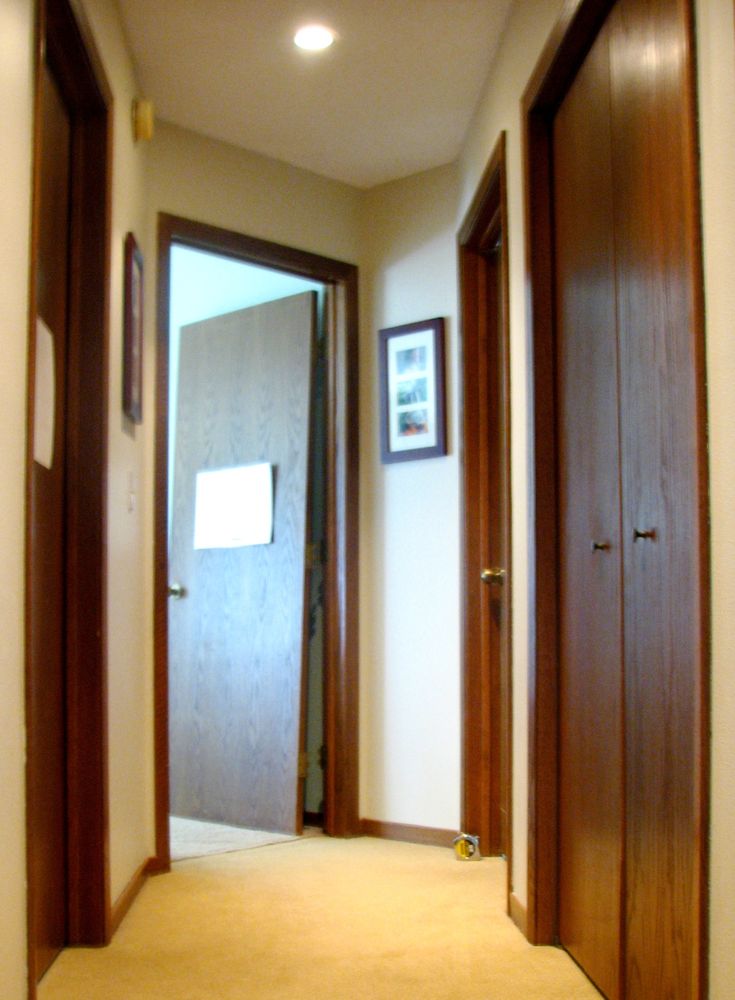 an empty hallway with wooden doors and pictures on the wall above it, along with carpeted flooring