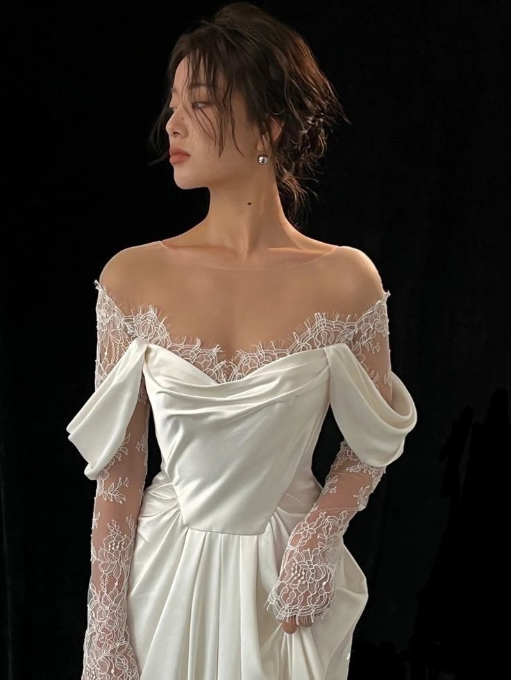 a woman in a white dress with long sleeves and lace on her arms, standing against a black background