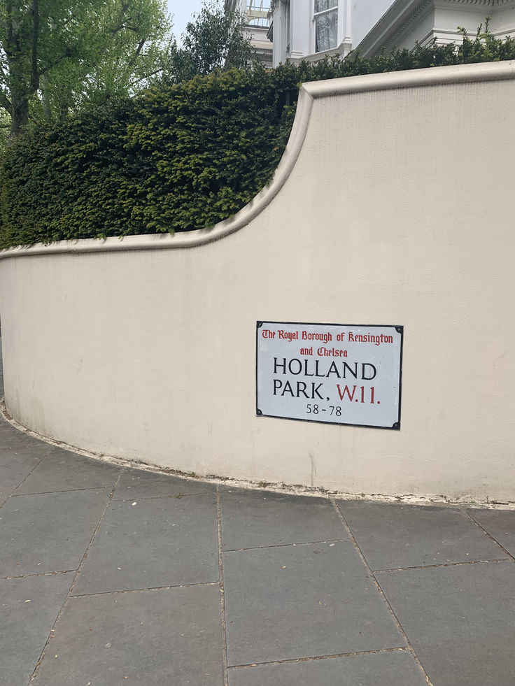 a sign on the side of a building that says holland park, w1 and is next to a hedge