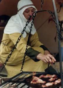 a woman cooking food on top of a grill with chains hanging from it's sides