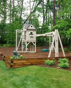 a wooden play set in the middle of a yard with trees and grass around it