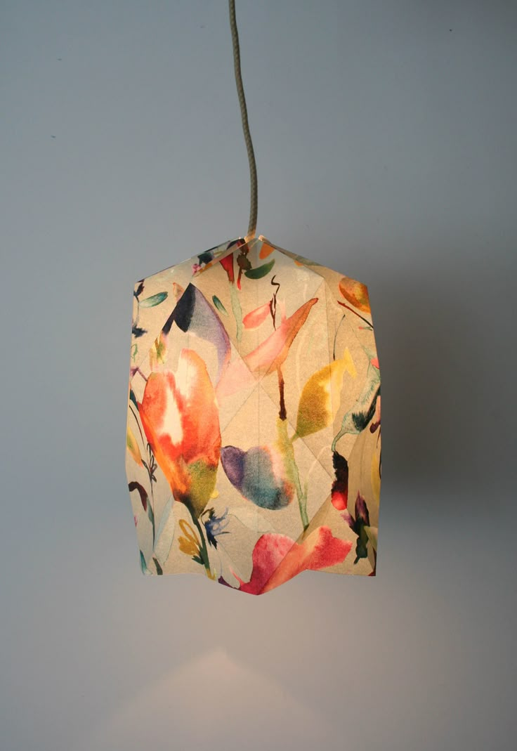 a lamp that is hanging from a cord on the wall with flowers printed on it