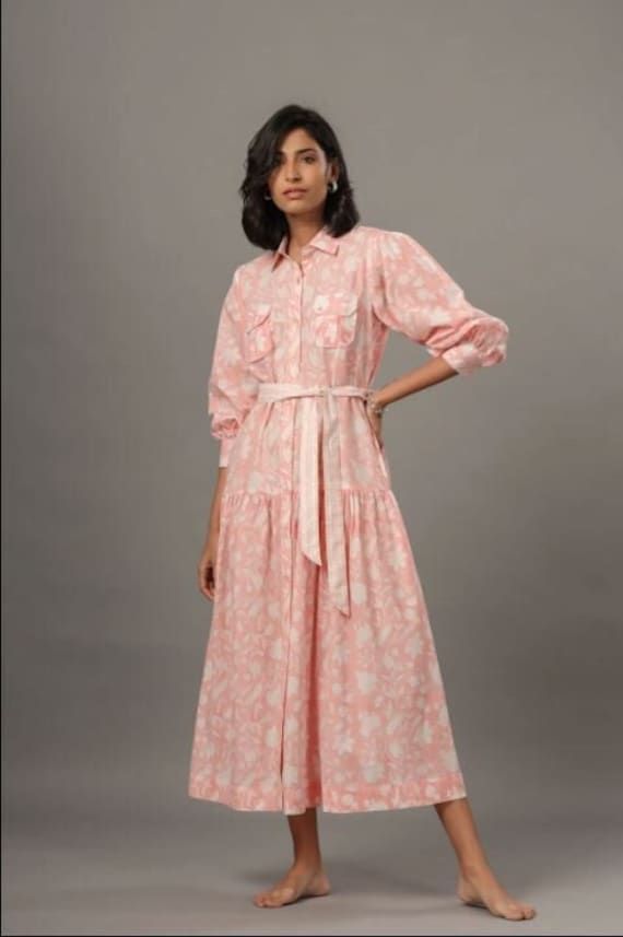 Made of breathable cotton, this pink shirt dress is a perfect spring/summer look. Beautifully hand block printed, with subtle ruffle details and a removable belt completes this feminine look. Delicate Hand wash Feminine Spring Cotton Shirt Dress, Feminine Cotton Shirt Dress For Spring, Long Sleeve Pink Cotton Shirt Dress, Pink Long Sleeve Cotton Shirt Dress, Spring Cotton Belted Shirt Dress, Cotton Belted Shirt Dress For Spring, Belted Cotton Shirt Dress For Spring, Feminine Long Sleeve Cotton Shirt Dress, Summer Cotton Shirt Dress With Ruffles