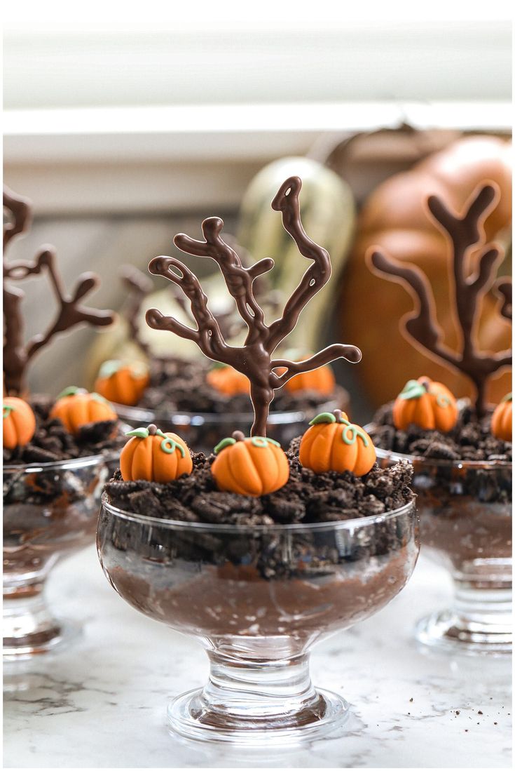 desserts in glass bowls with fake trees and pumpkins on top, sitting on a table