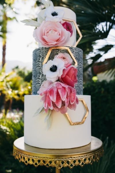 a three tiered cake with pink flowers on the top and gold trimmings