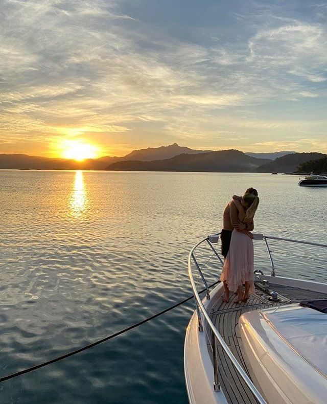 two people standing on the deck of a boat at sunset