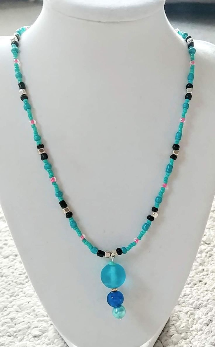 This necklace is made with blue seed beads, turquoise seed beads, silver spacer beads, pink seed beads, and a blue bauble in the middle. Toggle clasp. Measures 18 inches long end to end. Turquoise Beaded Dangle Necklaces With Tiny Beads, Turquoise Dangle Beaded Necklaces With Tiny Beads, Blue Dangle Beaded Necklace With Tiny Beads, Blue Baubles, Toggle Clasp, Spacer Beads, In The Middle, Seed Beads, Turquoise Necklace