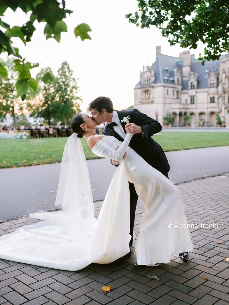 a bride and groom kissing in front of a large building on a brick walkway outside