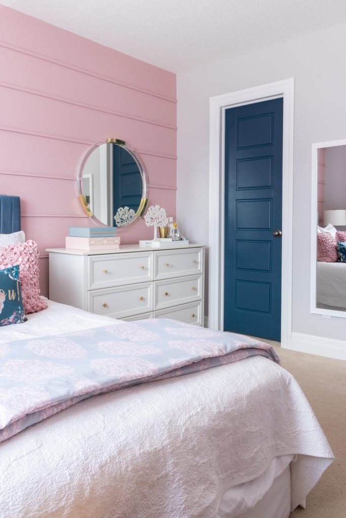 a bedroom with pink walls and blue doors, white bedding, and dressers