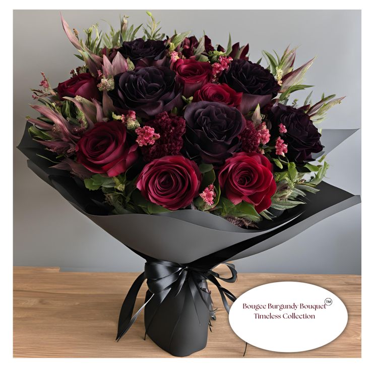 a bouquet of red and purple roses in a black paper wrapper on a wooden table