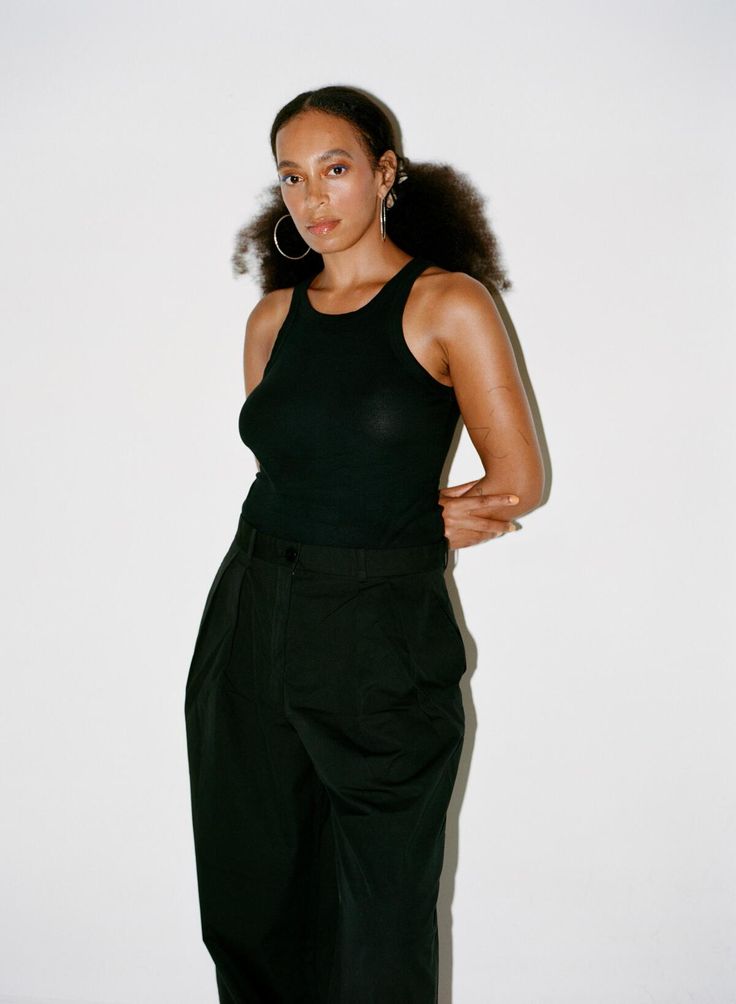 a woman standing in front of a white wall wearing black pants and a tank top