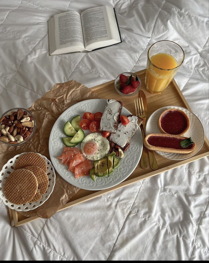 a tray filled with food on top of a bed next to a glass of orange juice