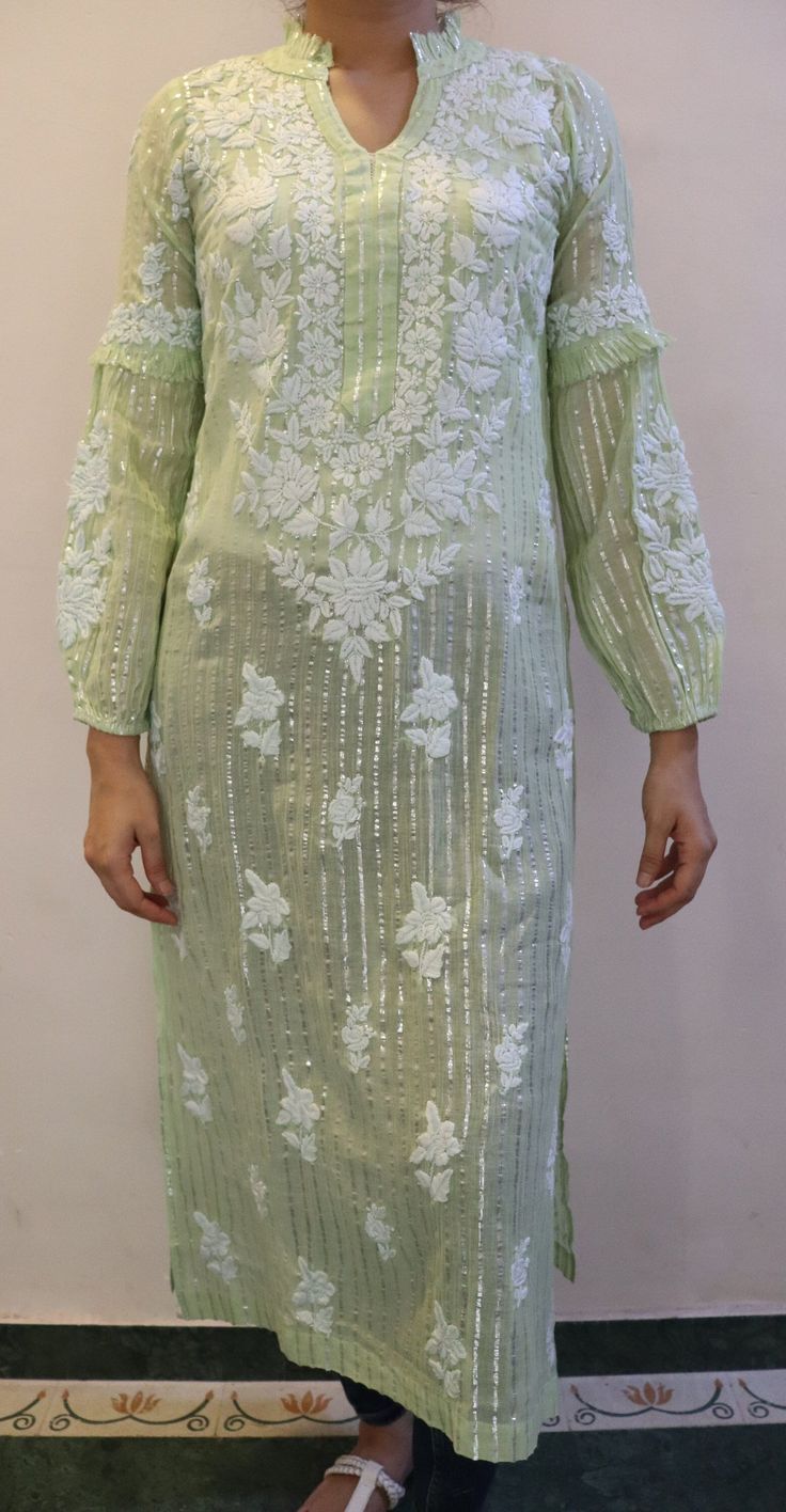 This Exquisite tunic combines the timeless charm of Chikankari embroidery with the contemporary allure of cotton and lurex fabric. Its  a perfect blend of traditional craftsmanship and modern style. With its intricate detailing of ruffled collar, balloon sleeves, beautiful embroidery and subtle shimmer, this tunic adds a touch of elegance to any outfit. Lightweight and comfortable, its ideal for both casual and festive occasions. The addition of lurex threads enhances the tunics allure, creating a subtle shimmer that catches the light and adds a modern twist to the classic Chikankari style.  Made from 100% pure cotton Mulmul. Length - 46/47 inches Sizes -  S - fits bust 34 M - fits bust 36 L - fits bust 38 XL - fits bust 40 0X - fits bust 42 1X - fits bust 44 Prewashed. Preshrunk. Summer Embroidered Cotton Silk Kurta, Spring Cotton Silk Kurta With Zari Work, Embroidered Cotton Silk Kurta For Summer, Spring Wedding Kurta With Mirror Work, Elegant Straight Kurta Tunic With Floral Embroidery, Spring Designer Wear Cotton Silk Dress, Long Sleeve Cotton Silk Kurta With Embroidered Sleeves, Cotton Silk Kurta With Embroidered Sleeves, Bollywood-style Fitted Kurta With Embroidered Sleeves