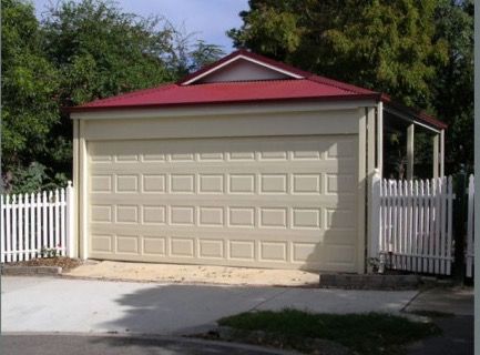 a garage with a red roof next to a white fence