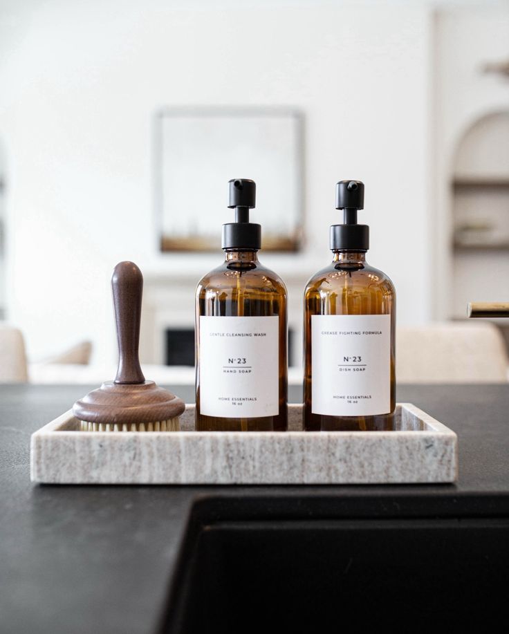 two bottles of hand soap sitting on top of a wooden tray next to a brush