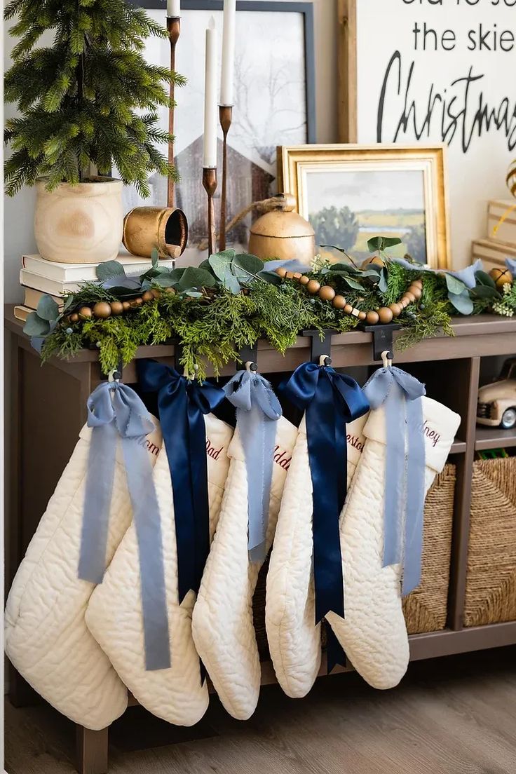 stockings are hung on the mantle with blue bows and greenery in front of them