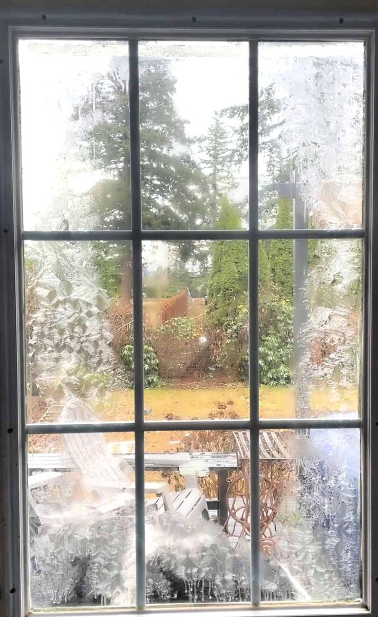 an open window with frost on the glass and trees in the back ground behind it