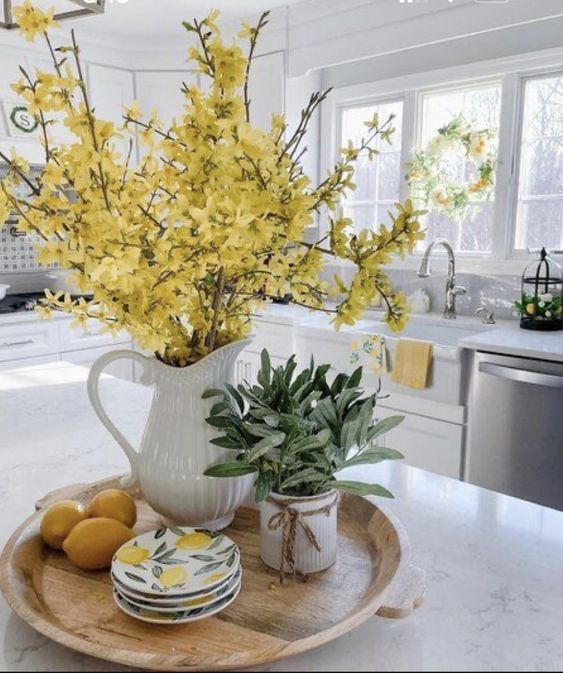 a white pitcher filled with yellow flowers sitting on top of a wooden tray next to plates