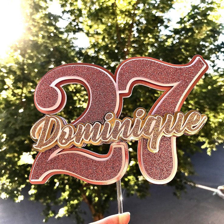 a pink cake topper with the number twenty five in gold and red sparkles