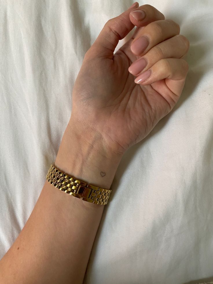 a woman's hand resting on top of a white sheet with gold bracelets