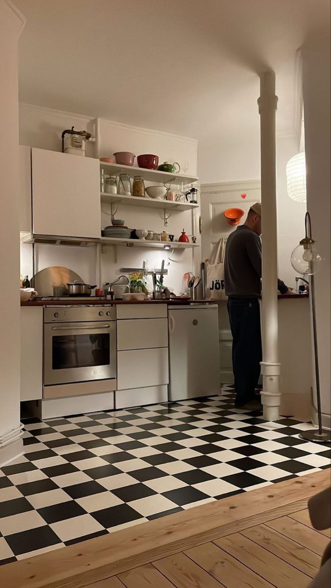 a man standing in a kitchen next to a black and white checkered floor