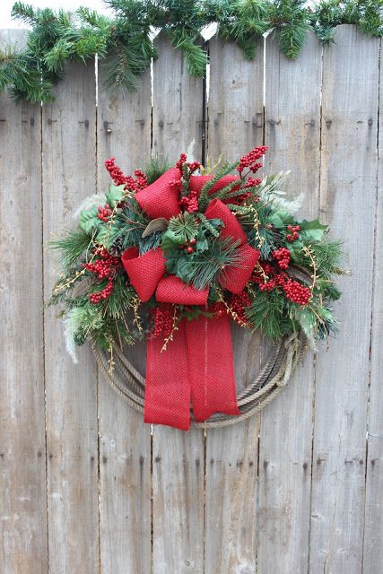 a wreath with red bows and greenery hanging on a fence