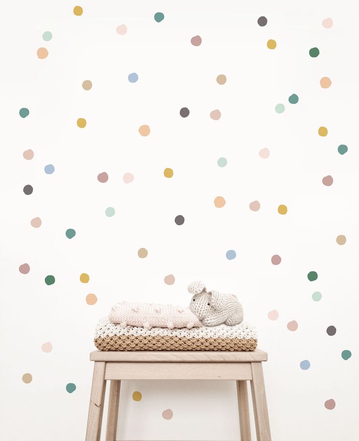 a baby's room with polka dot wallpaper and a wooden stool in the foreground