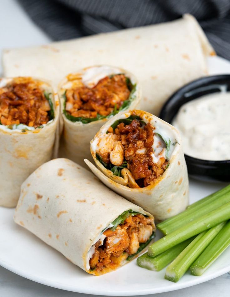 several burritos on a plate with celery and dip