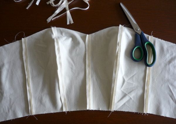 some scissors are laying on top of white fabric and paper with strips of thread next to it