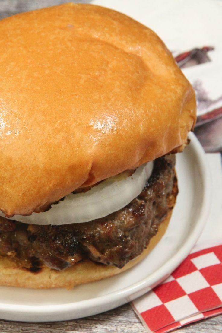 a hamburger with meat and onions on a bun is sitting on a checkered tablecloth