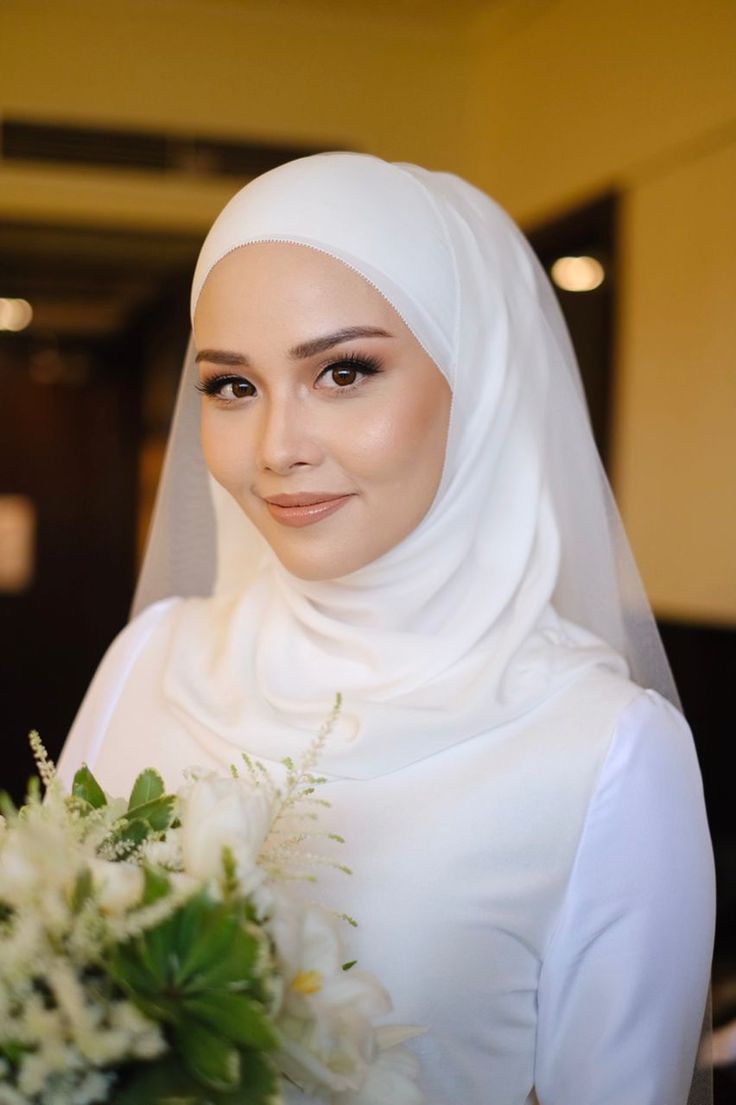 a woman wearing a white hijab holding a bouquet of flowers