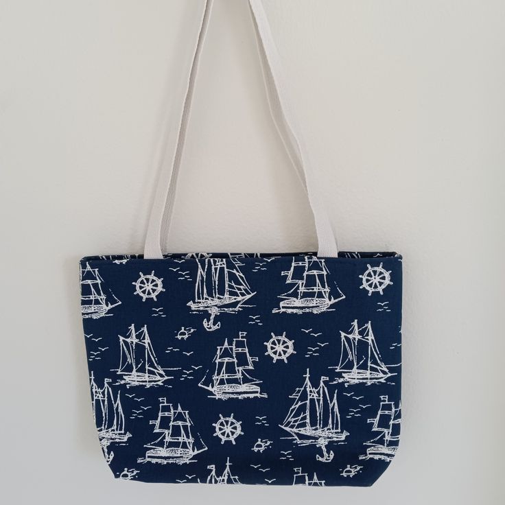 Navy blue canvas tote with white sail boats. Measures 14" wide, 12 1/2" tall, 4" deep. White web straps with 15" drop. Fully lined in solid navy. Top zip to secure your items. Inside pocket. Everyday Nautical White Bag, White Nautical Everyday Bag, White Nautical Bag For Everyday, Nautical Canvas Bags For Everyday Use, White Nautical Canvas Bag, Nautical White Canvas Bags, White Nautical Canvas Bags, Nautical Beach Bag In Sail Color, Everyday Nautical Canvas Bags