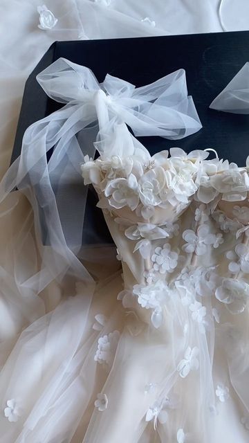 wedding dress laying on top of a black box with white flowers and ribbon around it