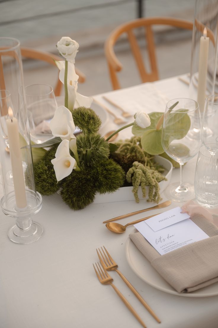 the table is set with white flowers and place settings