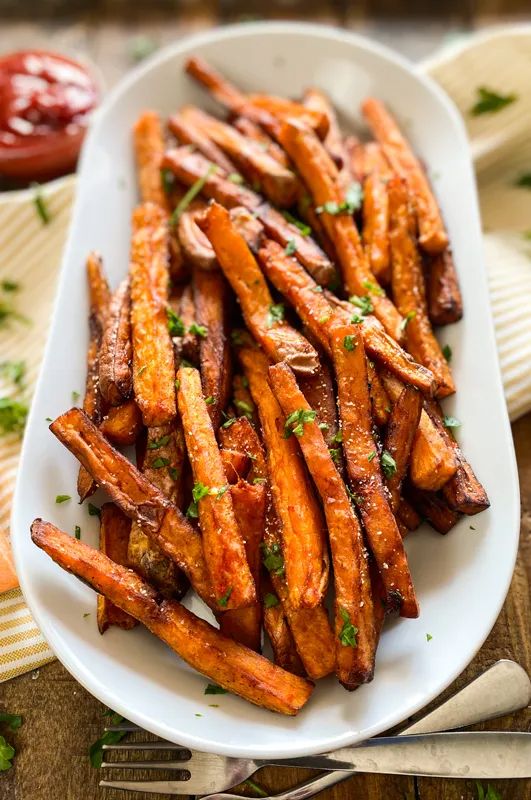 baked sweet potato fries on a white plate with parsley and ketchup in the background