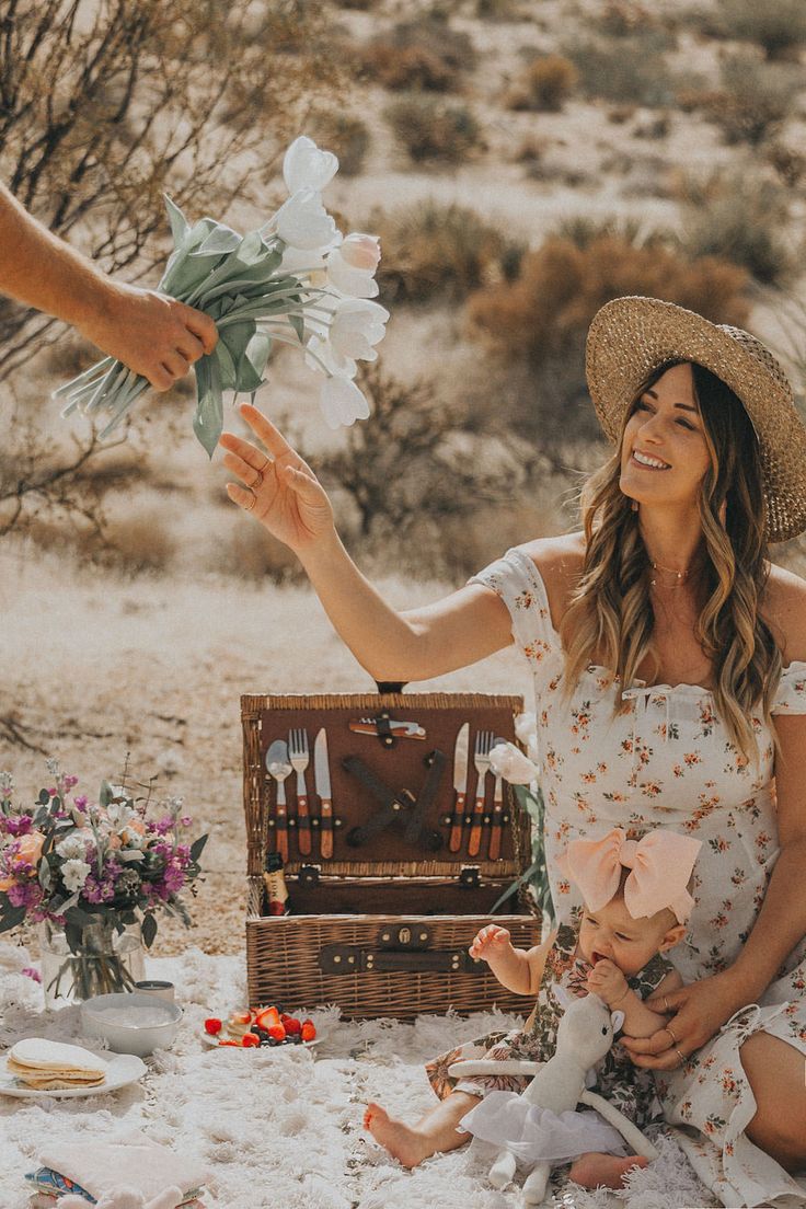 a woman sitting on the ground with flowers in her hand and a man holding a baby